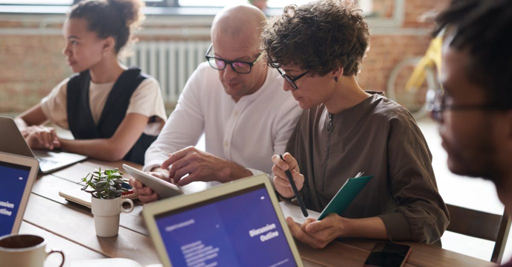 A group of adults working together on laptops and tablets in a modern office setting.